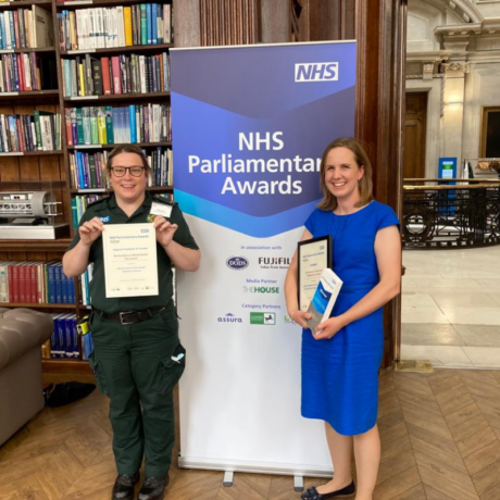 Carly from the LAS mental health team and Georgina from the End of Life care team holding their certificates in front of a banner that reads NHS Parliamentary Awards