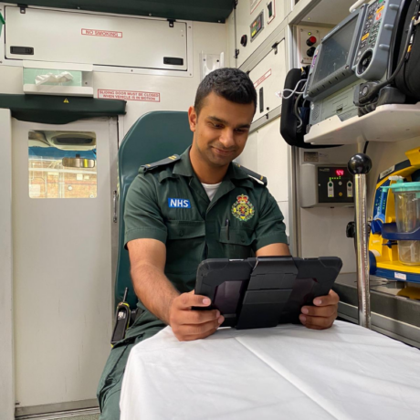 A medic sat on a seat in the back of an ambulance uses an iPad