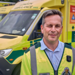 Daniel Elkeles in a LAS top in front of a row of ambulances