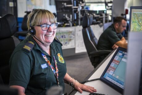 Mandy smiling at her desk with a headset and looking towards a screen in the control room