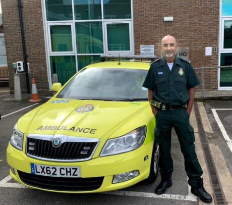 Paramedic Raj Mann stood in uniform next to an ambulance car