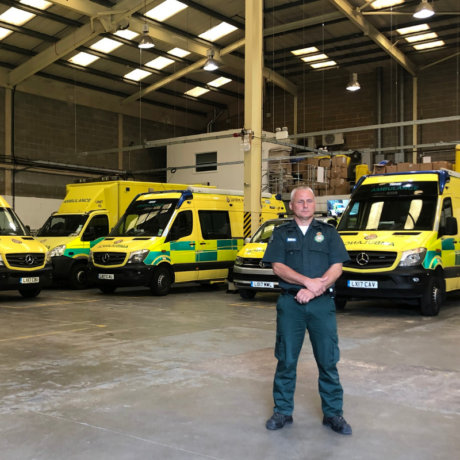 Stuart posing for a picture with ambulance vehicles behind him
