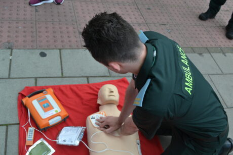 An ambulance medic shown performing chest compressions on a mannequin, with a defibrillator next to the mannequin