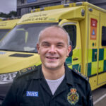 Dr John Martin in uniform in a picture in front of a row of ambulances