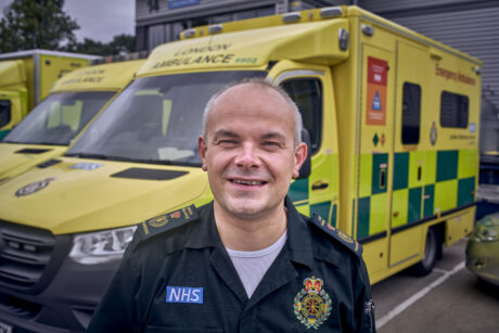 Dr John Martin in uniform in a picture in front of a row of ambulances