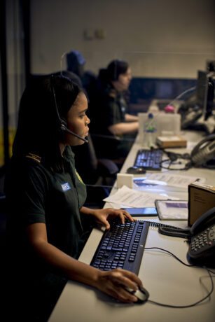 Two call handlers at their workstation wearing uniform and headsets taking calls