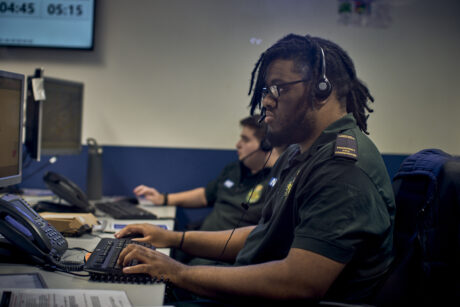 Two call handlers at their workstation wearing uniform and headsets taking calls