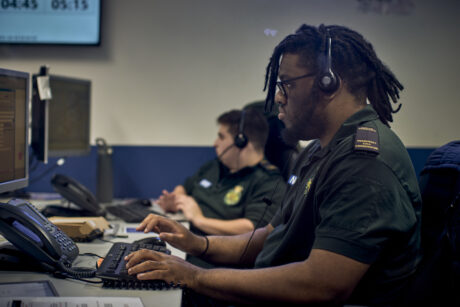 Two call handlers at their workstation wearing uniform and headsets taking calls
