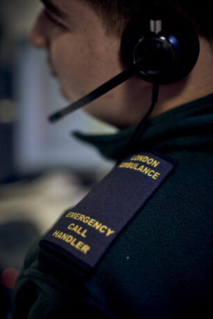 A call handler with a headset and their epaulettes which read London Ambulance Emergency Call Handler