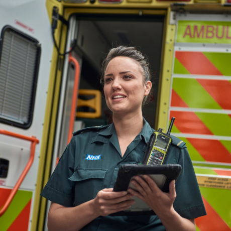 A medic holding an iPad with an open ambulance rear door behind her