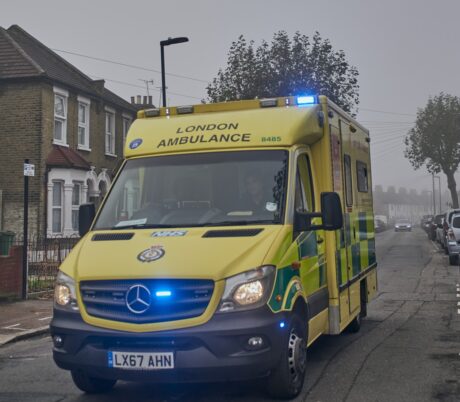 An ambulance with flashing blue lights on a road on a wintry cloudy day