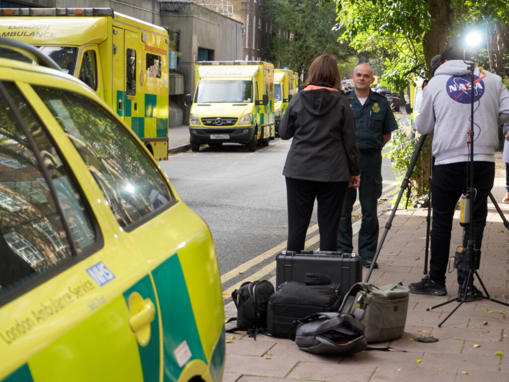 An image of a person in LAS green uniform being interviewed by a reporter with a camera filming to the side