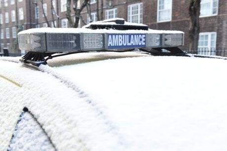 An ambulance vehicle with a dusting of snow across the windscreen, blue lights and side doors