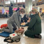 A medic watches as a person performs chest compressions on a dummy