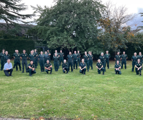 A large group of medics in uniform posing for a group photo in a field with trees behind