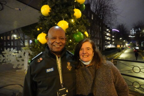 John standing smiling next to the Christmas tree with wife Carol