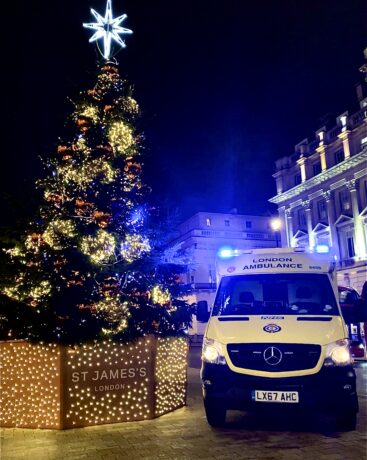 An ambulance with flashing lights next to a large Christmas tree