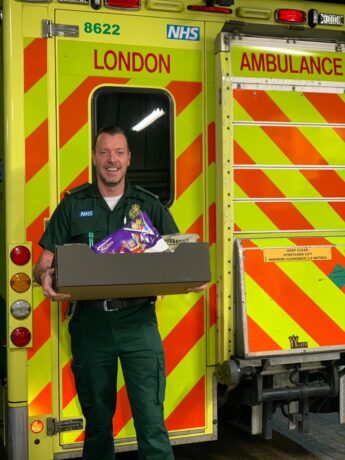 Nigel holding a box of donated items behind an ambulance