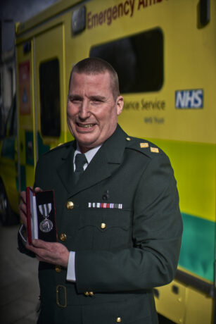 Jason in dress uniform holds his medal photographed in front of an ambulance