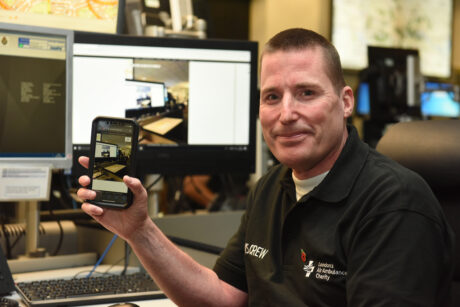 Jason in the 999 control room holding a phone showing the GoodSam instant on scene video platform in use