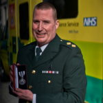 Jason in dress uniform holds his medal photographed in front of an ambulance