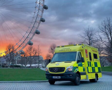 Ambulance parked in front of London Eye with sunset in background