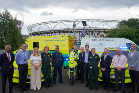 Attendees standing in front of 7 new green vehicles with the Olympic stadium in the background.