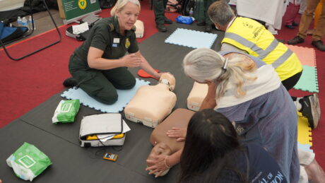 LAS staff demonstrating how to perform CPR on a mannequin with two members of public listening