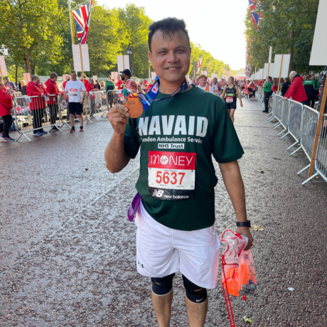 A marathon runner raising money for London Ambulance Charity holds up his medal. 
