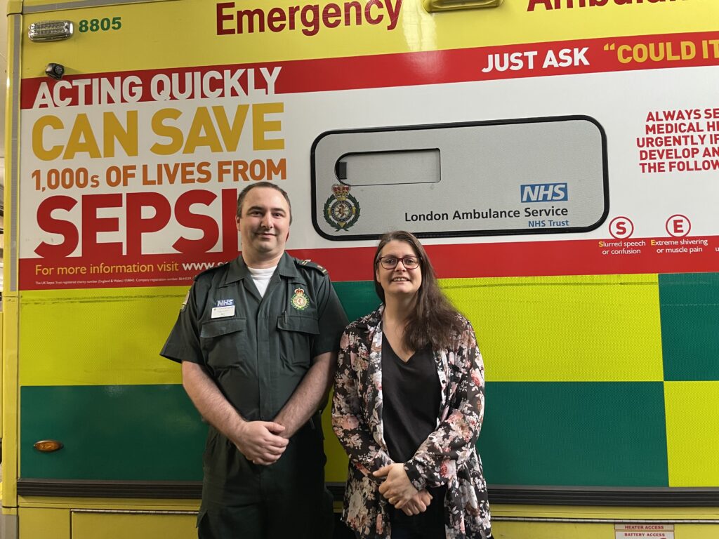 A picture of Benjamin Butto and Melissa Mead in front of a London Ambulance with Sepsis messaging on it. 