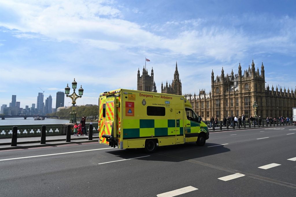 A picture of an ambulance driving across a bridge in central London with the Palace of Westminster in the background. 