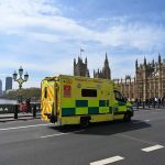 A picture of an ambulance driving across a bridge in central London with the Palace of Westminster in the background.