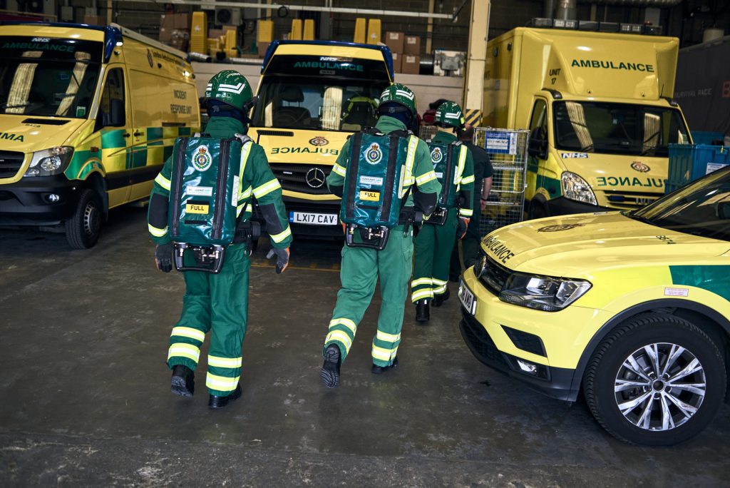 A picture of three HART paramedics in special protective uniforms, with lots of ambulance vehicles visible in the background. 