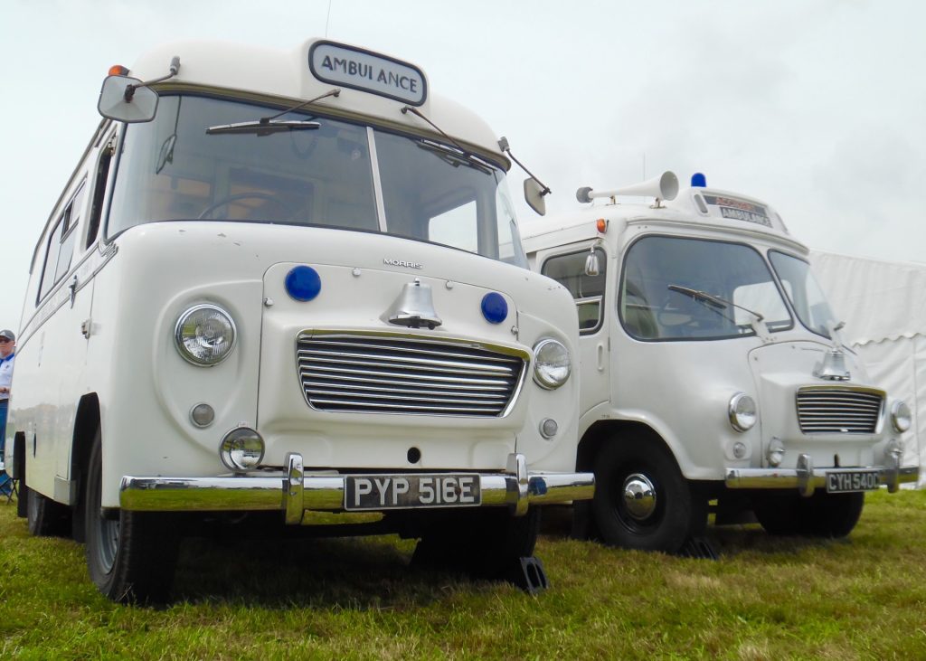Image shows two historic ambulances parked in a field.