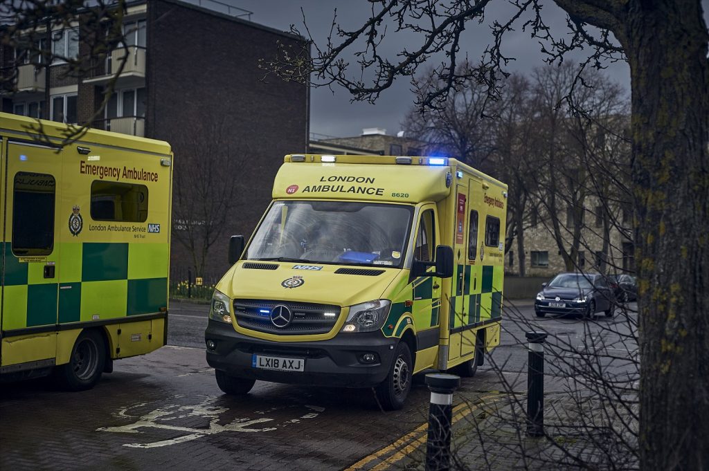 An ambulance on blue lights driving in dark and stormy weather.