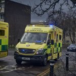 An ambulance on blue lights driving in dark and stormy weather.