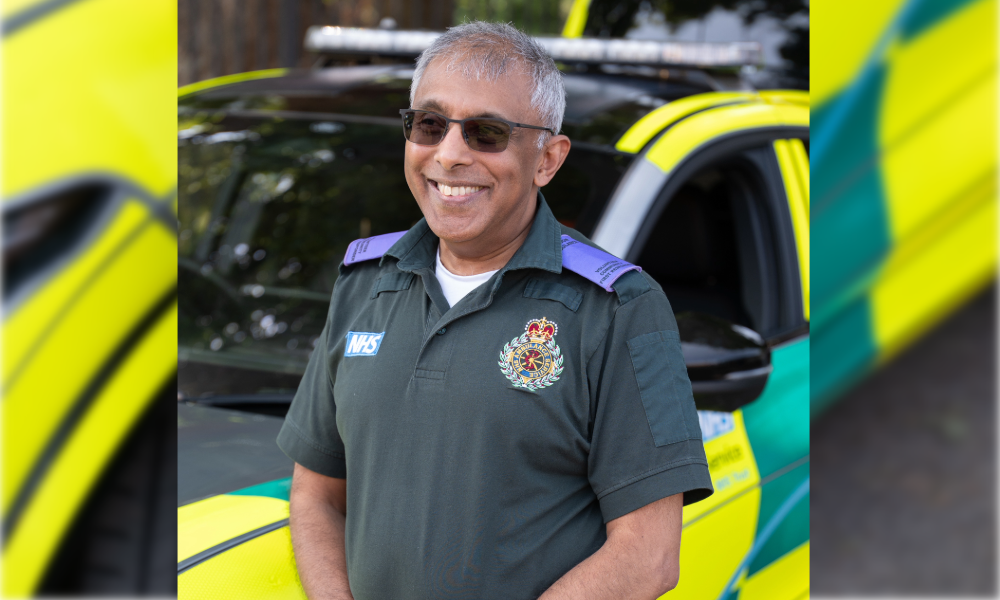 A community first responder in their uniform, standing in front of a London Ambulance vehicle.