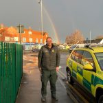 Paramedic Andy posing in front of a rainbow and next to a fast response ambulance