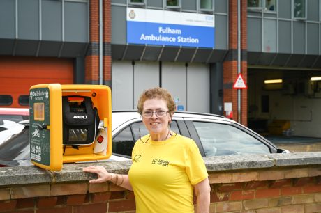 Carolyn standing in-front of a defibrillator outside of Fulham Ambulance Statio